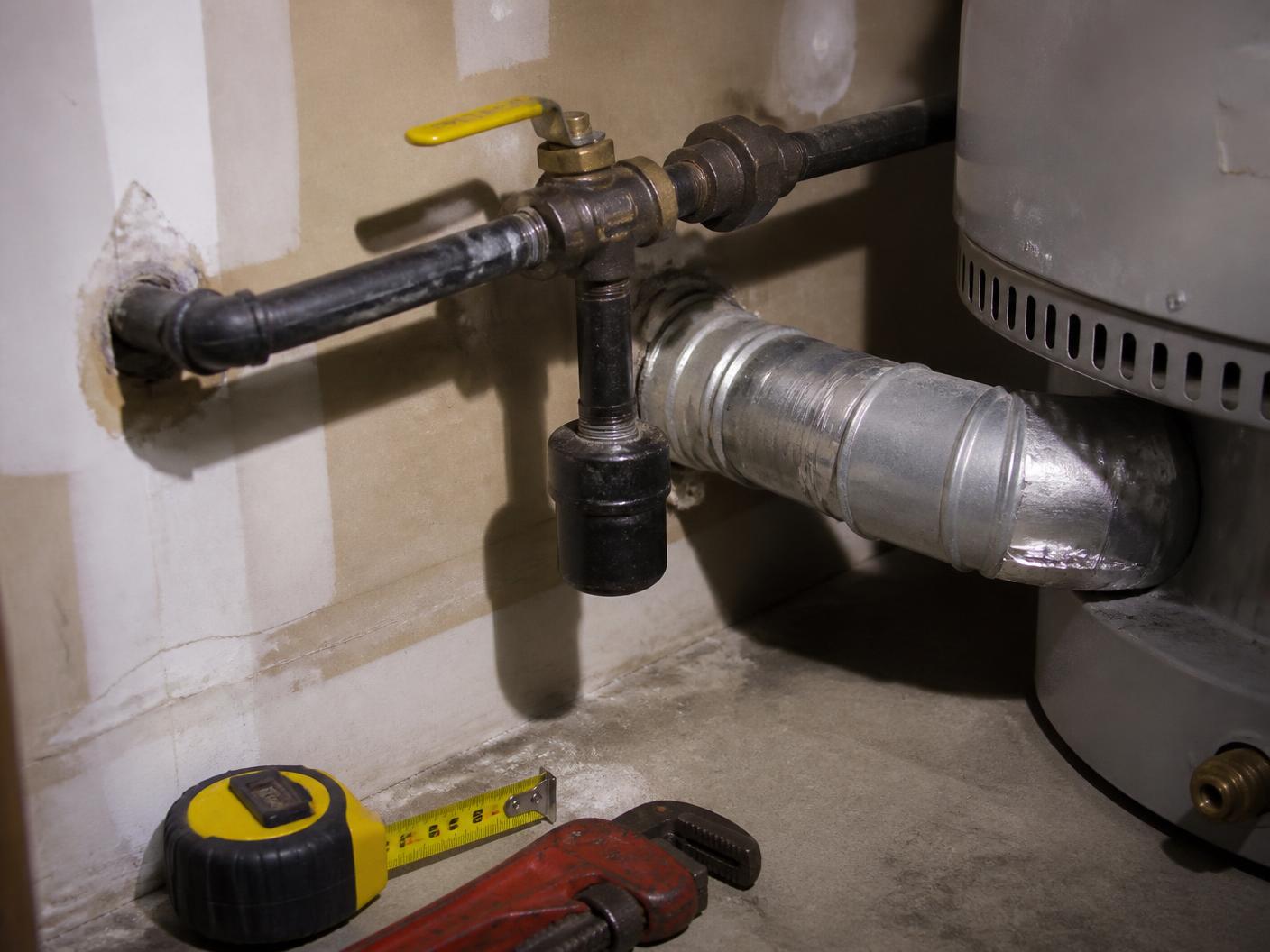 Black iron gas piping with a yellow shutoff handle, sediment trap, and galvanized flue vent connector at a water heater